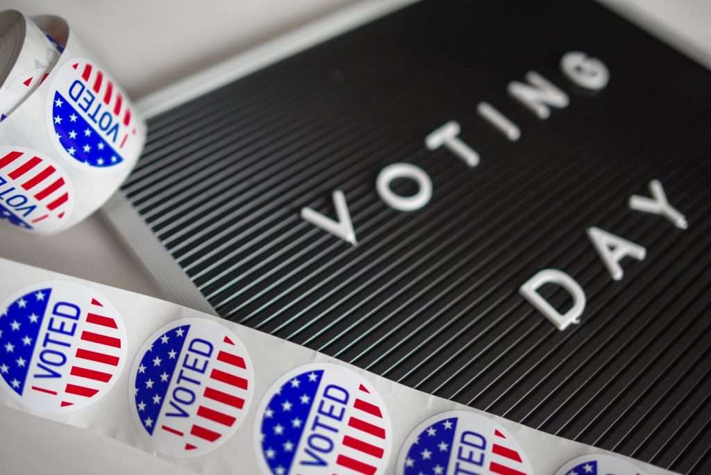 A roll of Stars & Banners Voted stickers slightly unfurledon a partially obscured Voting Day board