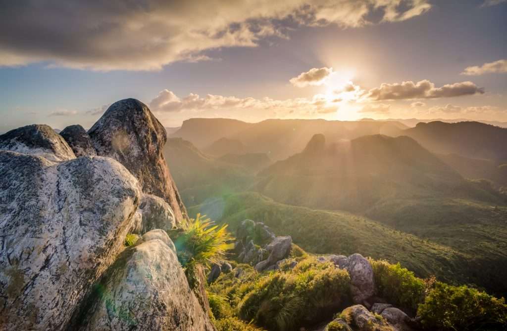 Gray stone formation overlooking green hills during sunrise