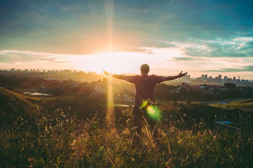 Man on a hill with arms outstretched, welcoming a bright sunrise: a new dawn.